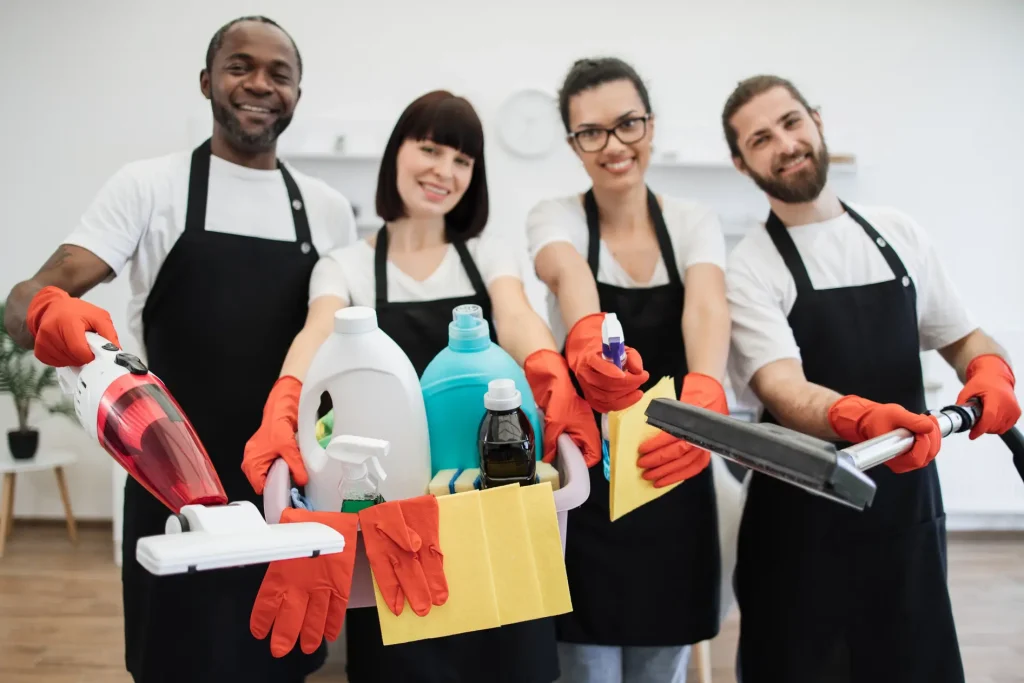 Four professional cleaners from Diamond Touch Cleaners smiling confidently at the camera while holding various cleaning products and tools